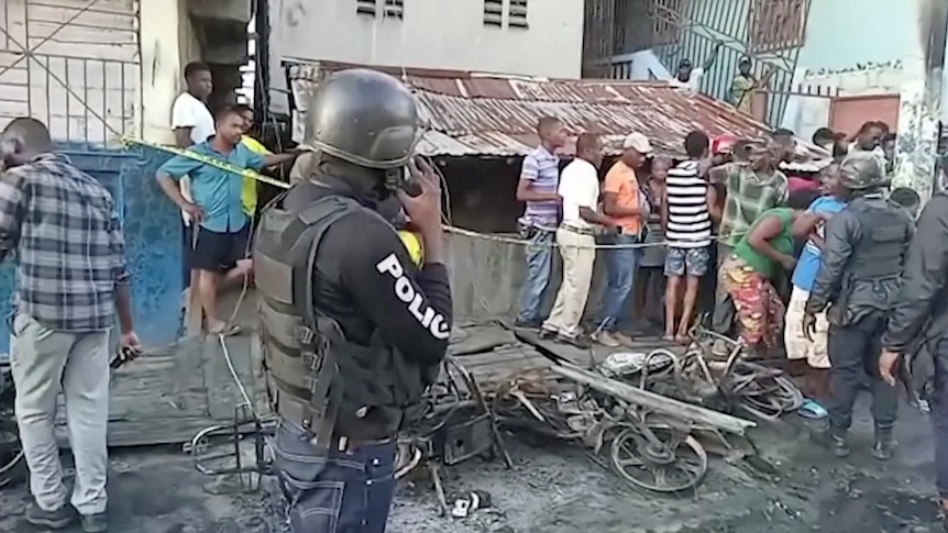 Oameni și un ofițer de poliție măcina în jurul locului exploziei din Cap-Haitien, Haiti, 14 decembrie 2021.