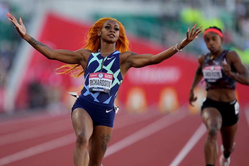A US female sprinter crosses the finish line with her arms raised.