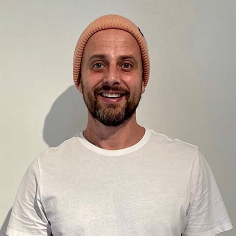 A young man in a beanie and white tshirt smiles