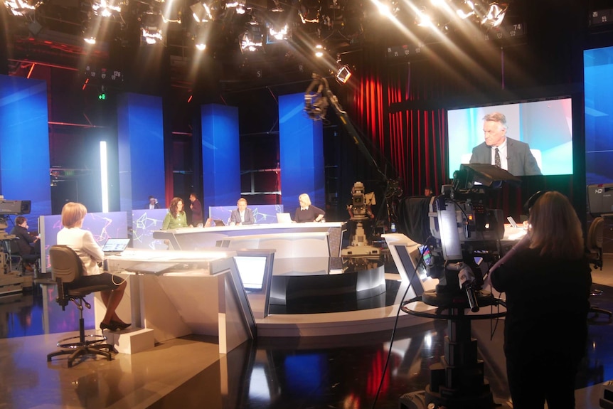 Wide shot journalists sitting at desk in studio.