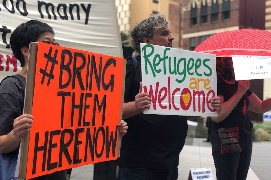 Protesters hold signs saying 'refugees are welcome' and 'bring them home'.