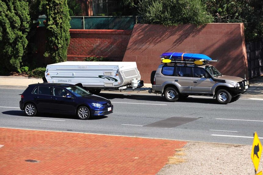 A four-wheel drive with a camper trailer and kayaks on a freeway