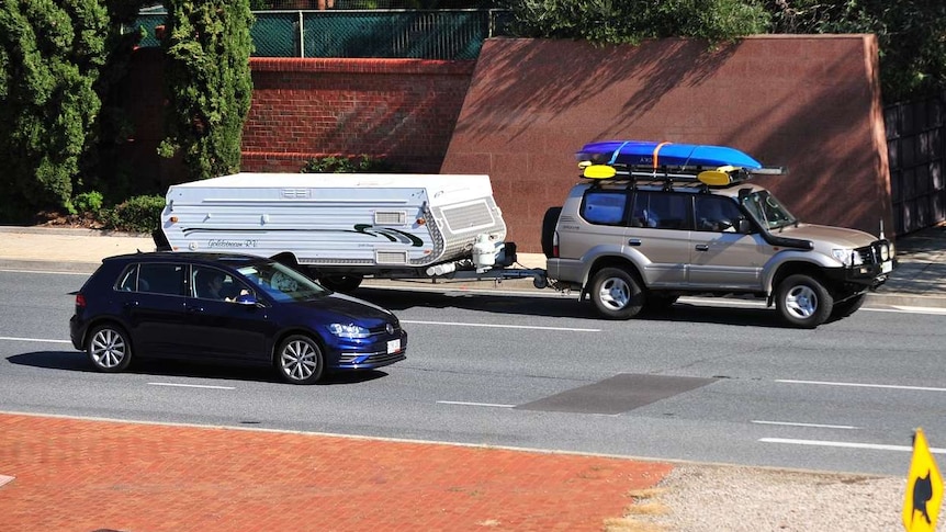 A four-wheel drive with a camper trailer and kayaks on a freeway