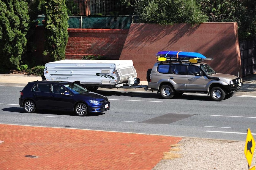 A four-wheel drive with a camper trailer and kayaks on a freeway