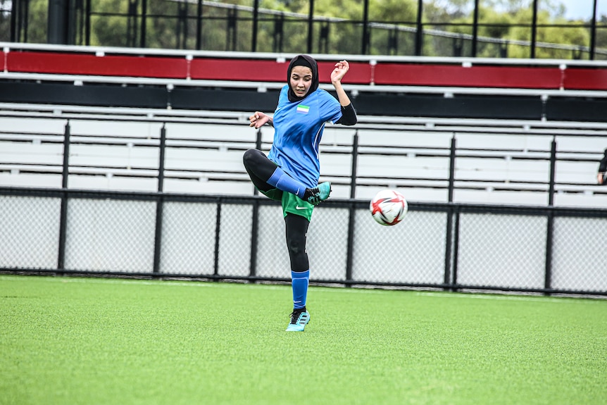 A footballer kicks the ball, she's standing on one leg, with the other raised high in the air.