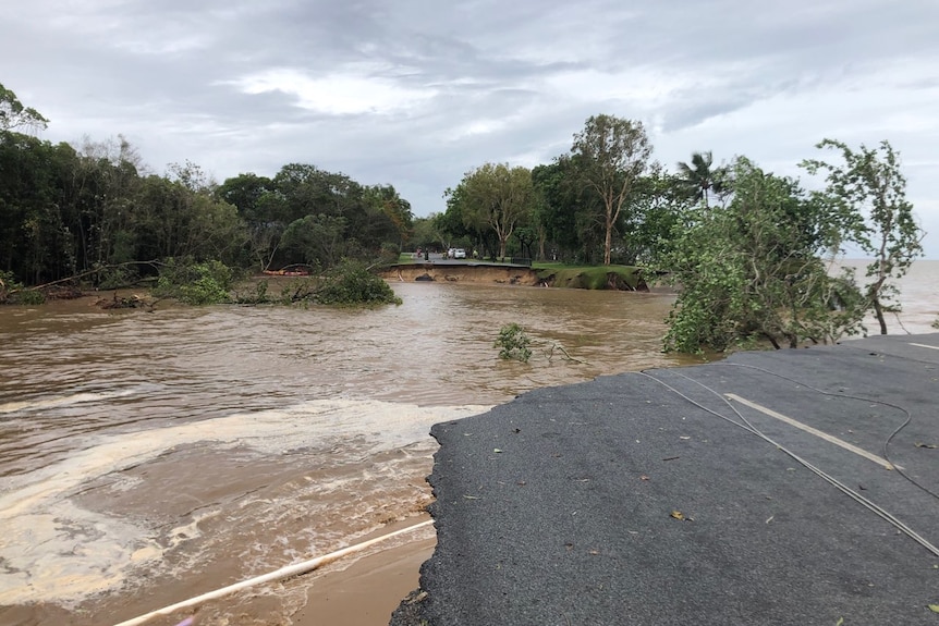 A 30-metre section of the road pavement on Holloways Beach esplanade completely missing with flood water rushing through