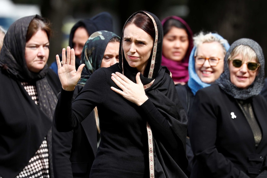 Jacinda Ardern dressed in a head scarf surrounded by Muslim women