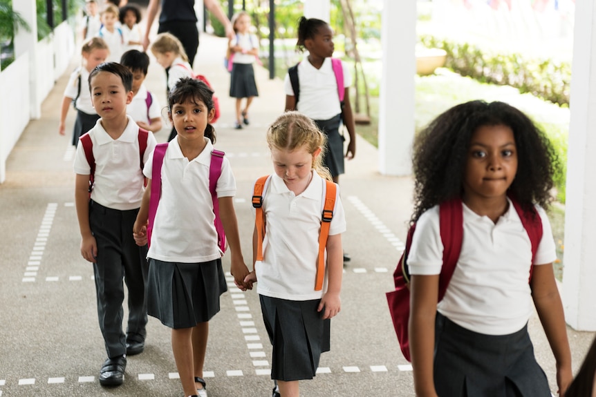 a group of children in uniform with three of them holding hands.