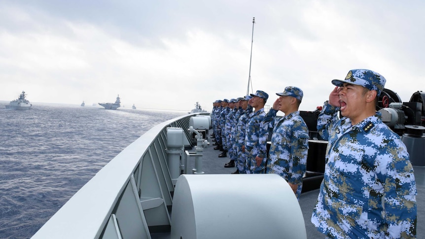 Chinese soldiers on a vessel look towards sea and salute.