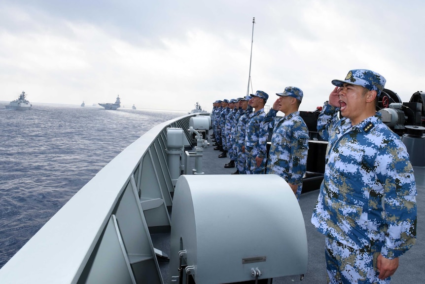 Chinese soldiers on a vessel look towards sea and salute.