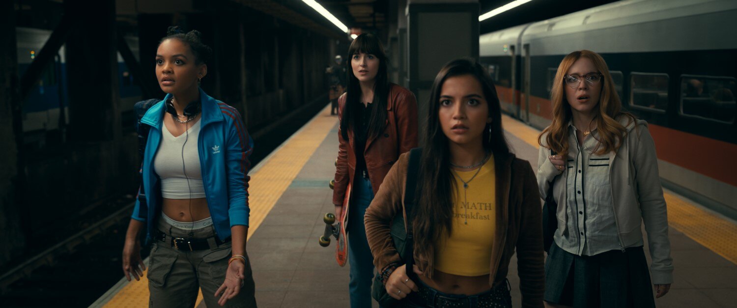 Four young woman stand on a subway platform, all facing one direction looking shocked, in action shot from Madame Web movie.