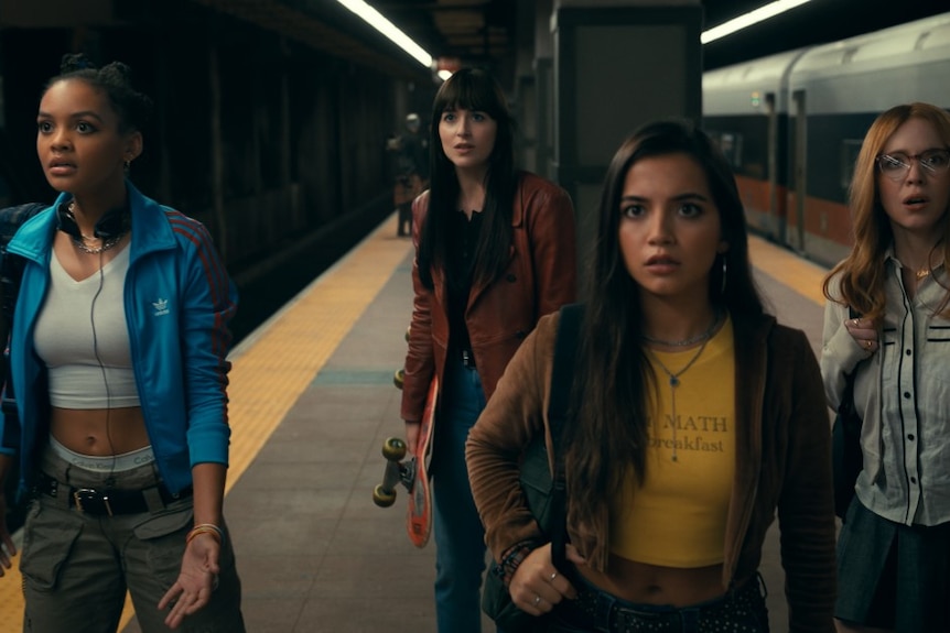 Four young woman stand on a subway platform, all facing one direction looking shocked, in action shot from Madame Web movie.