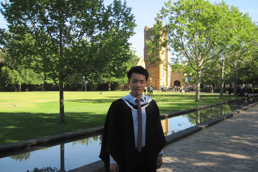 A young man in graduation robe standing inside Melbourne University 