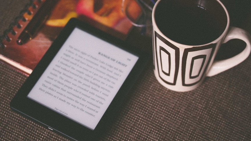 Ebook sits with a pen, pair of glasses and mug on a table