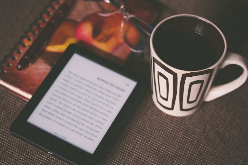 Ebook sits with a pen, pair of glasses and mug on a table