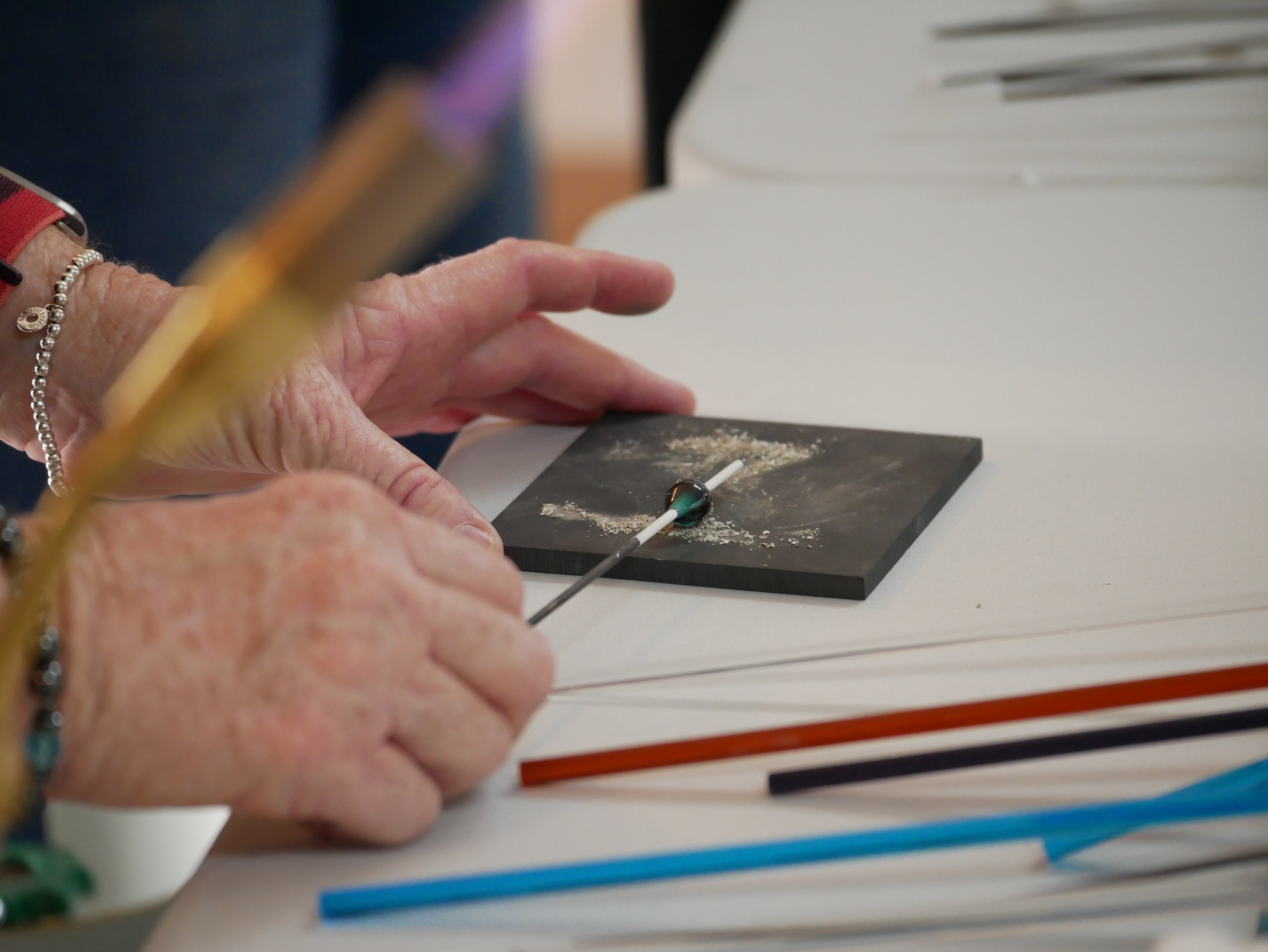 close up of hands rolling a molten glass bead through ashes