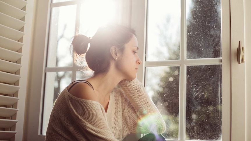Woman looks pensive while staring out a window.