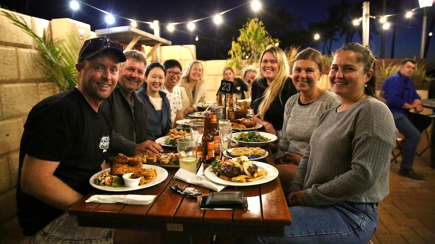 A group of people eat dinner at a table in a pub courtyard at night. 