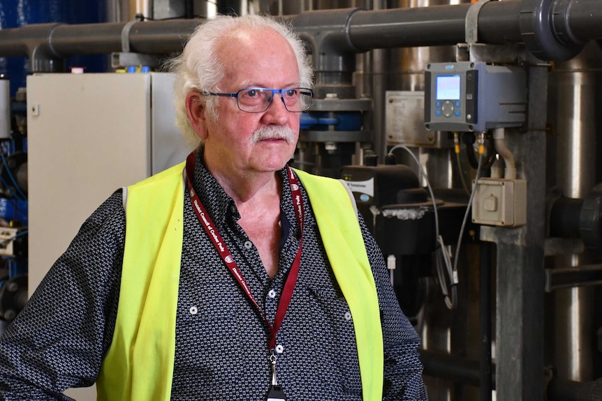 A man with glasses and white hair stands in an industrial area.