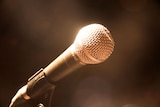 Stage light shines on a microphone, blurred and darkened background.