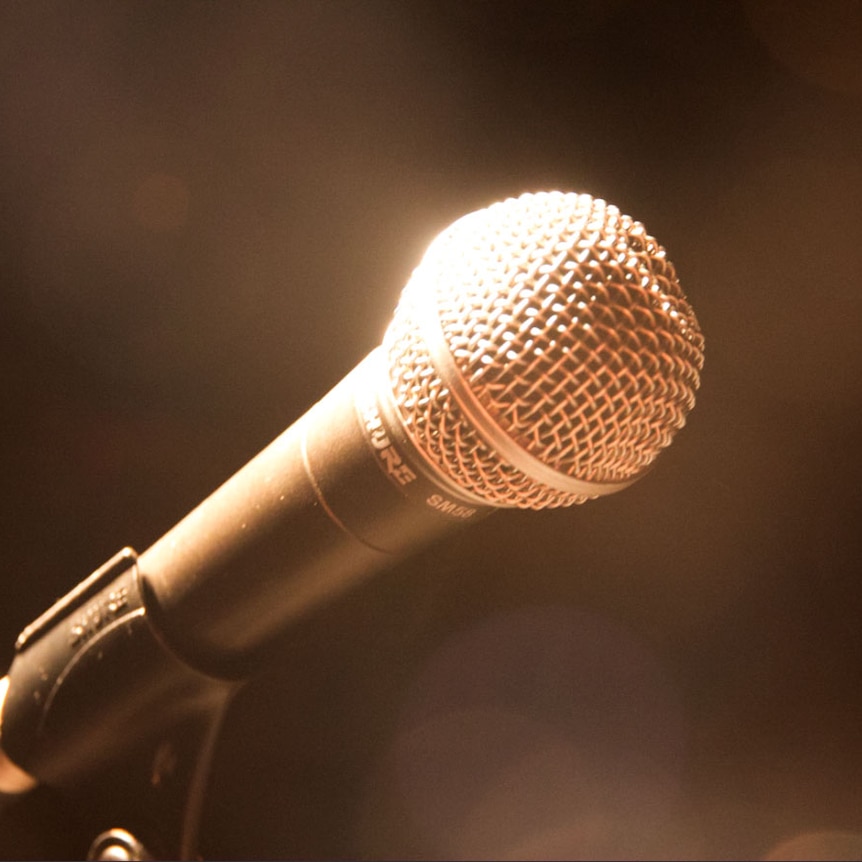 Stage light shines on a microphone, blurred and darkened background.