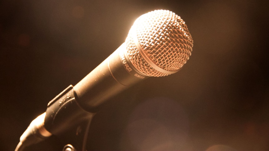 Stage light shines on a microphone, blurred and darkened background.