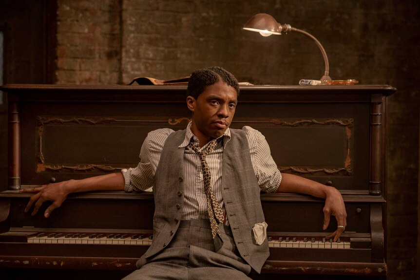 A scene from Ma Rainey's Black Bottom with Chadwick Boseman as a blues musician leaning against a piano