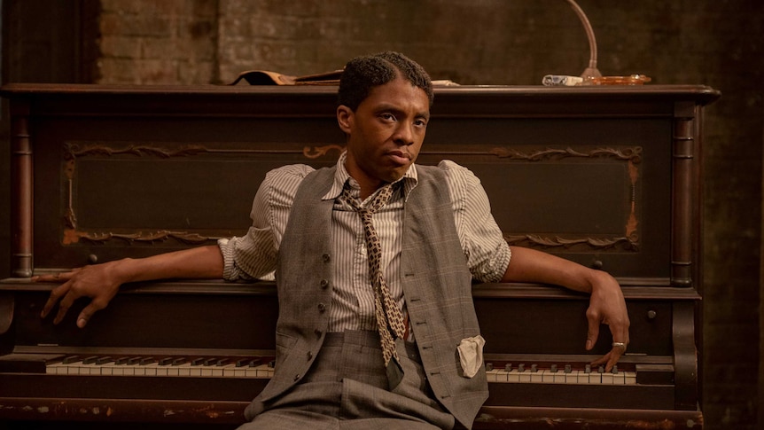 A scene from Ma Rainey's Black Bottom with Chadwick Boseman as a blues musician leaning against a piano