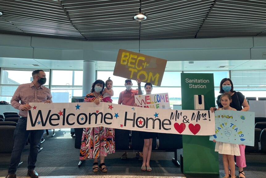 A family holding a sign saying 'Welcome home Mr and Mrs'