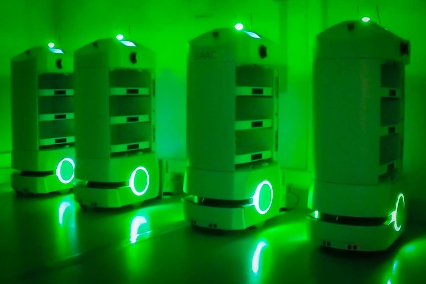 Four Automated Guided Vehicles are glowing green as they charge.