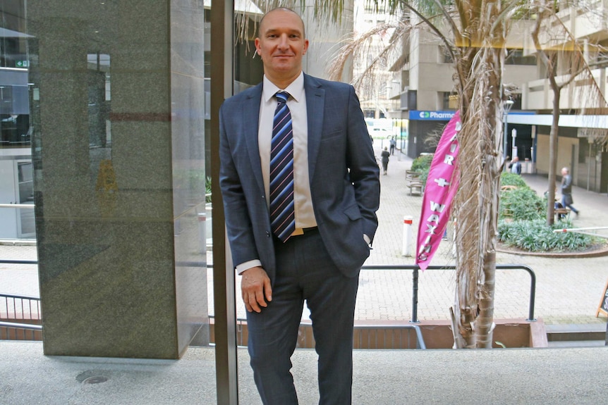 Andrew Bahr looks toward the camera as he leans on a narrow pillar.