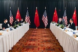Two desks facing each other with a US delegation behind one and a Chinese delegation behind another