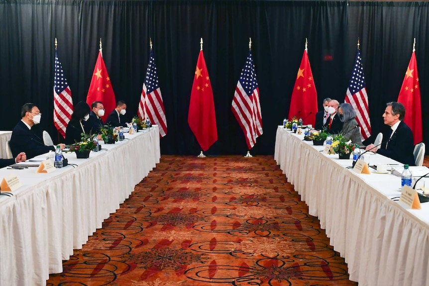 Two desks facing each other with a US delegation behind one and a Chinese delegation behind another