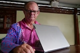 A man in a pink shirt with a laptop looking unimpressed