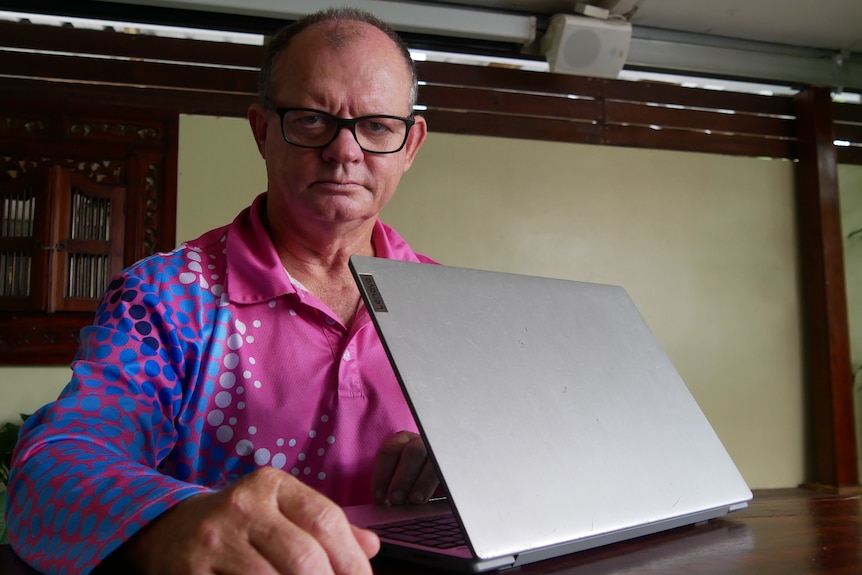 A man in a pink shirt with a laptop looking unimpressed