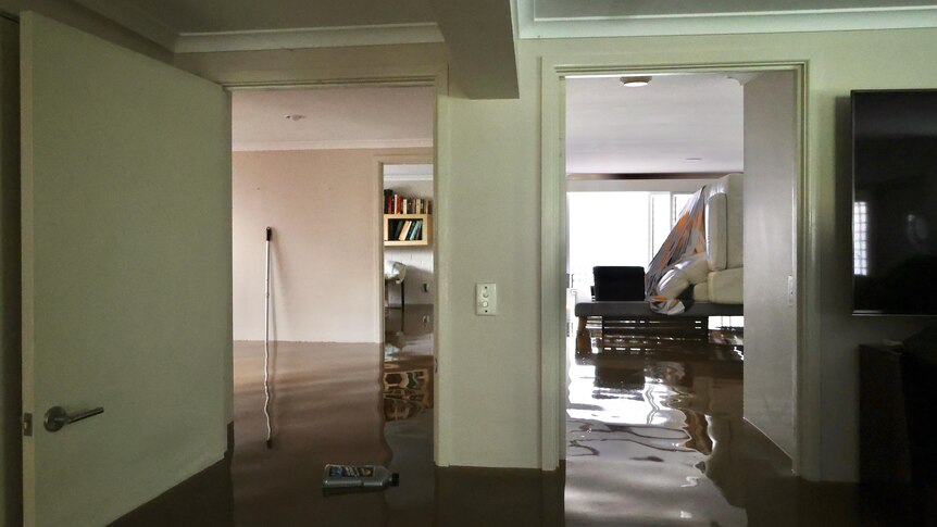 Water is at least one metre high inside a home, in one roome you can see couches stacked on a table. 