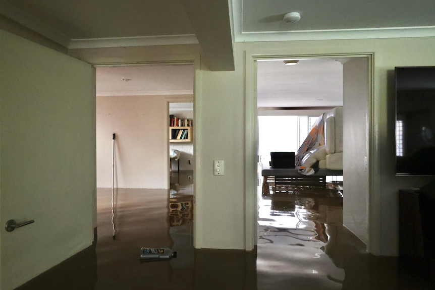 El agua tiene al menos un metro de altura dentro de una casa, en una habitación se pueden ver sofás apilados sobre una mesa. 