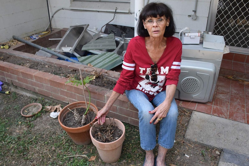 A woman sits outside her flood-damaged home