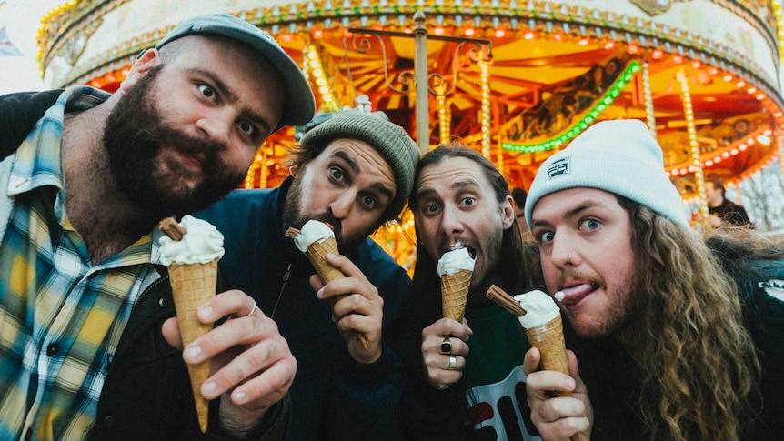 Four men lean in together in front of a horse carousel eating ice cream cones