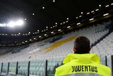 Juventus is written on the back of a steward's high-vis jacket as he looks at empty seats in a stadium.