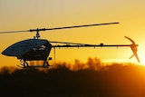 A helicopter drone flies at sunset