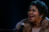 Aretha belts out a note into a microphone