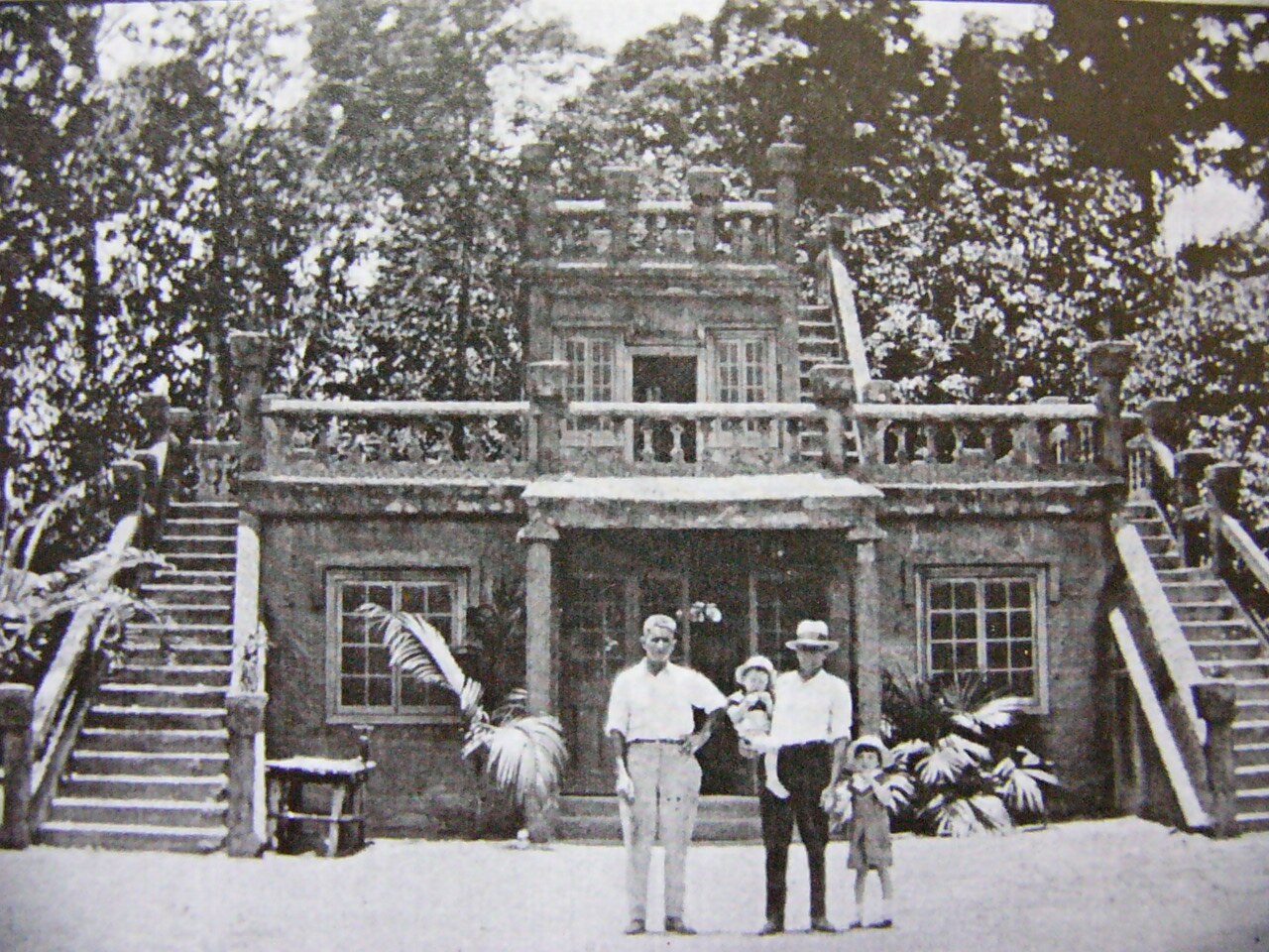 Una vieja fotografía en blanco y negro de dos hombres y dos niños parados frente a un castillo.