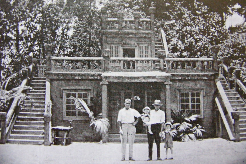 An old black and white photo of a two men and two children standing in front of a castle