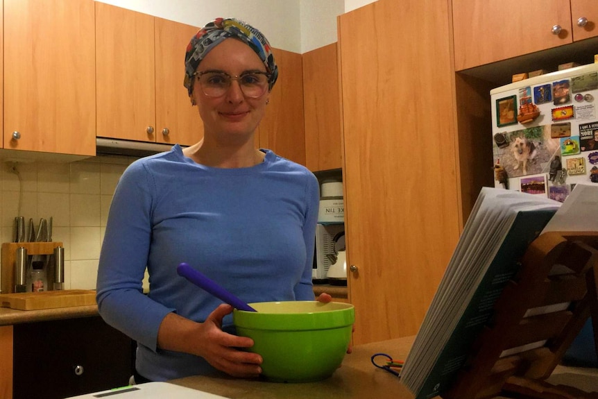 A young woman standing in her kitchen with a mixing bowl and scales