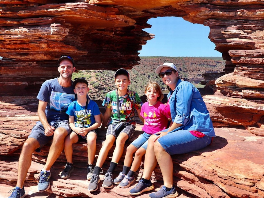 Family of five sitting on a red rock formation. 