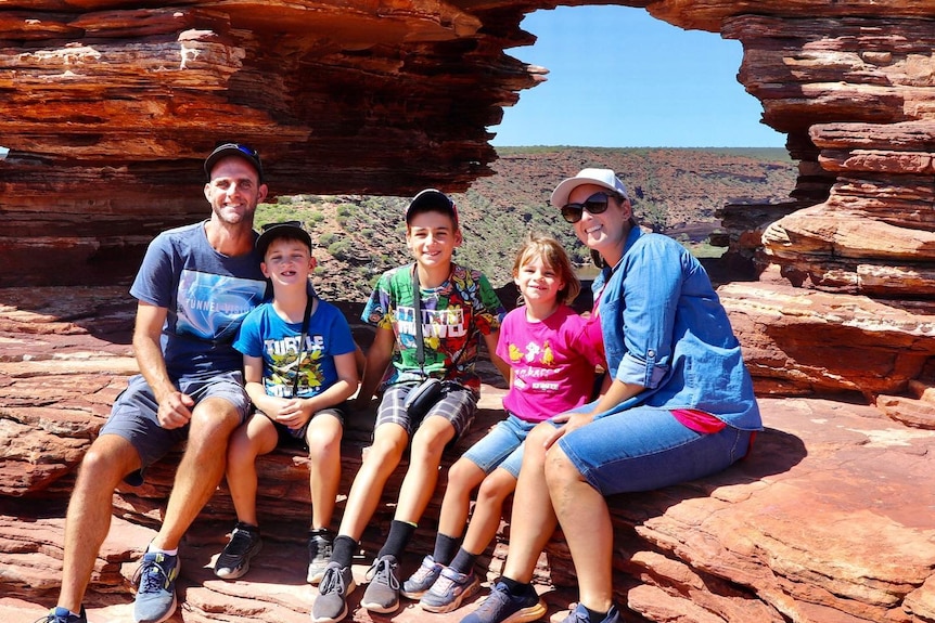 Family of five sitting on a red rock formation. 