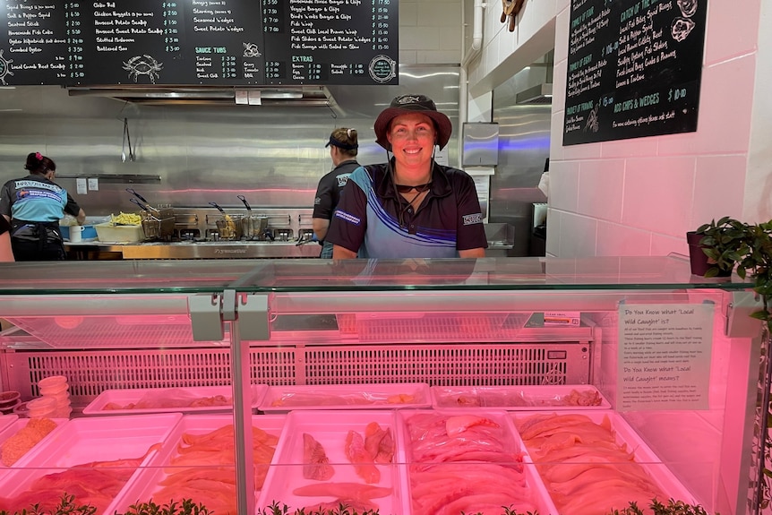 A woman smiles standing behind a counter at a fish and chip shop