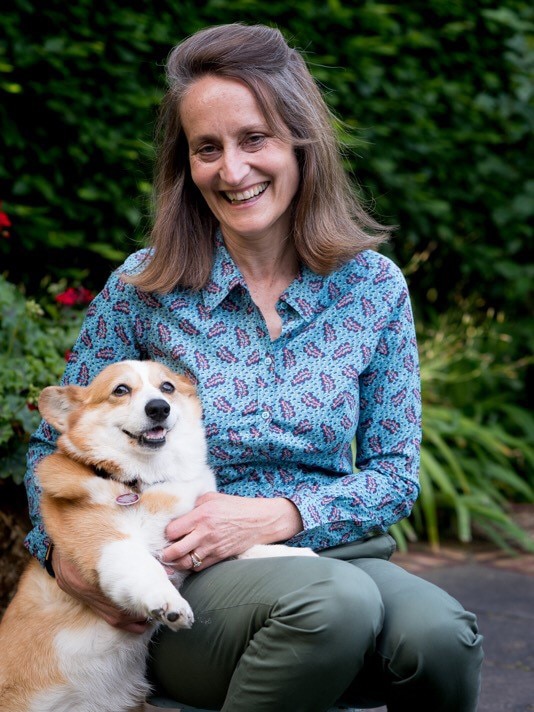 Clare Cannon sitting down in a garden setting holding a corgi.