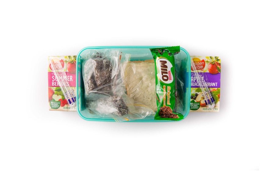 A peanut butter sandwich, lamingtons, chocolate rice puffs bar and two fruit drinks in a clear green lunch box.